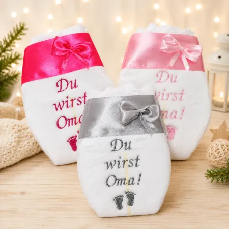 Bestickte Windel mit Aufschrift Du wirst Oma und rosa Satinband mit Punkten.